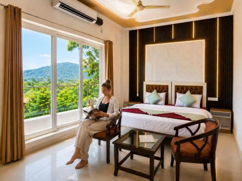 a woman sitting in a room with a bed and a window at Mountain View Retreat in Yog Tapovan in Rishīkesh