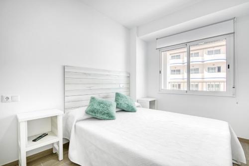 a white bedroom with a white bed with two blue pillows at Bonaire in Gandía