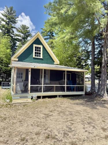 a house with a wrap around porch with trees at FRIENDLY INN LIMIT 5 cottage in North Sebago