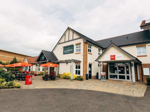 a building with tables and umbrellas in front of it at ibis Coleraine Riverside in Coleraine