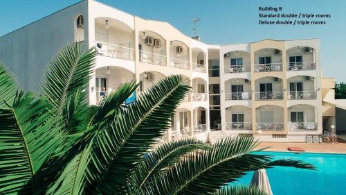 a large white building with a palm tree in front of it at Stavros Beach Hotel in Stavros