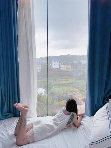 a girl laying on a bed looking out a window at Lyn's Hotel Da Lat in Da Lat