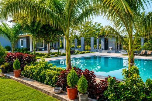 a swimming pool with palm trees and plants at Atithi Farms - 4 BHK Farm Villa with Private Pool in Thūr