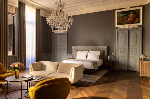 a bedroom with a bed and a couch and a chandelier at Margaret - Hôtel Chouleur in Nîmes