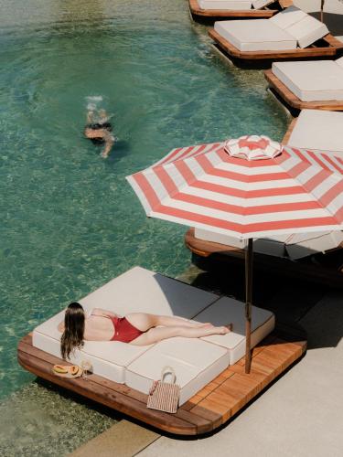 a woman laying on a bed under an umbrella in the water at Tropicana Suites & Villas Mykonos in Paradise Beach