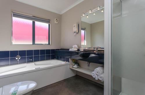 een badkamer met een bad, een wastafel en een toilet bij ASURE Albert Park Motor Lodge in Te Awamutu