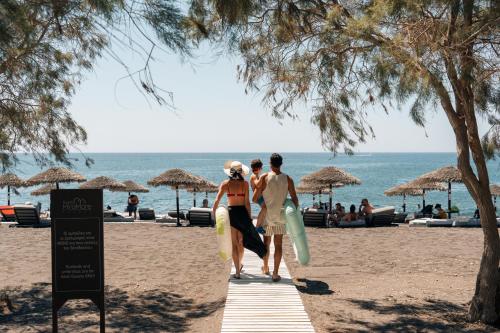 two people walking on the beach with their surfboards at Santo Miramare Beach Resort in Perivolos