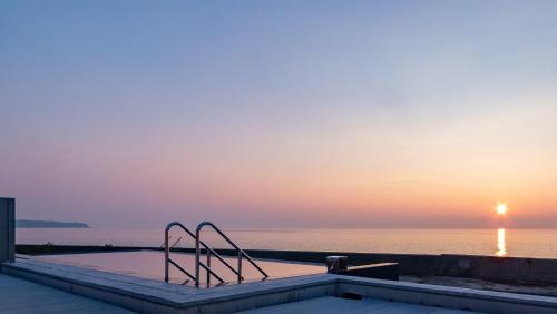 a swimming pool with a view of the ocean at sunset at Villa and Glamping Lazy Inn in Awaji
