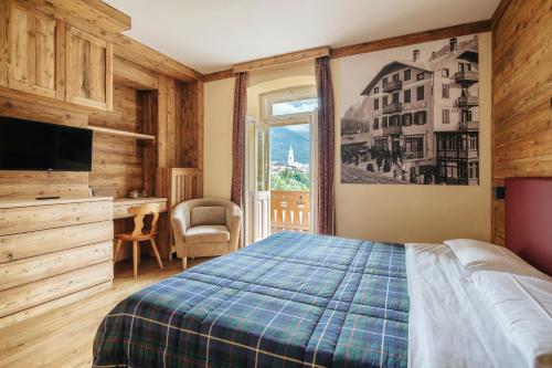 a bedroom with a bed and a desk and a window at Hotel Corona in Cortina dʼAmpezzo