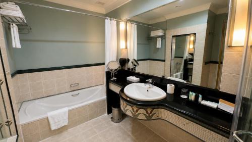 a bathroom with a sink and a tub and a mirror at Oryx Hotel in Abu Dhabi