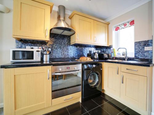 a kitchen with wooden cabinets and a washer and dryer at Sea Thrift in Port Isaac
