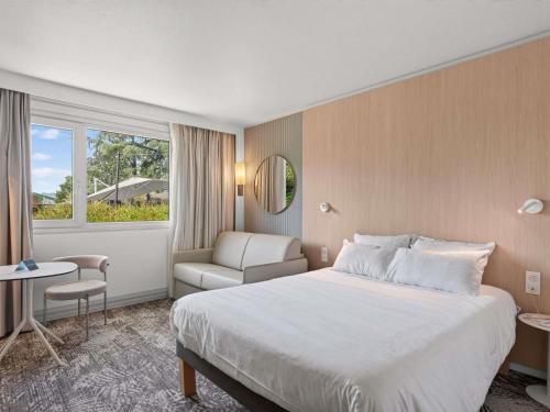 a hotel room with a bed and a chair at Novotel Pau Pyrénées in Lescar