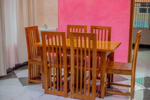 a wooden table with four chairs and a pink wall at MIAMi VILLA HOTEL in Mpanda
