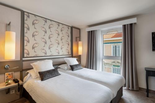 a hotel room with two beds and a window at Hotel America in Cannes