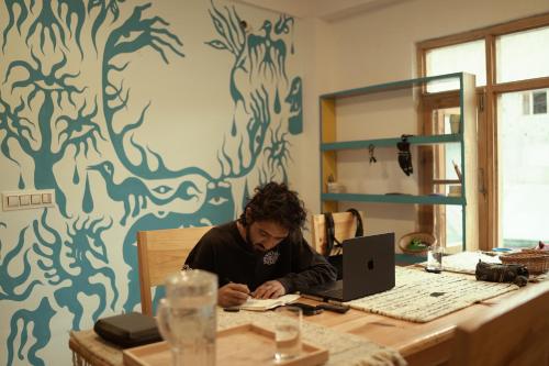 a man sitting at a table with a laptop computer at Sarai Stay in Kargil