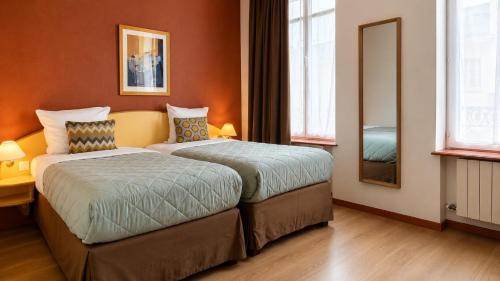 a hotel room with two beds and a mirror at Logis-Hôtel des Oliviers in Thionville