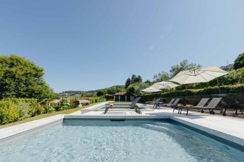a swimming pool with tables and chairs and an umbrella at Casas da Memória in Tarouca