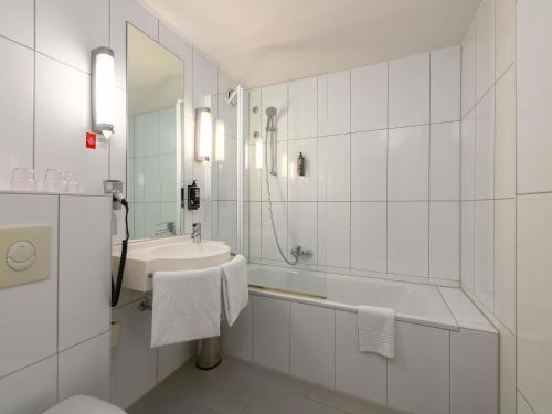 a white bathroom with a sink and a bath tub at ibis Nürnberg Hauptbahnhof in Nuremberg