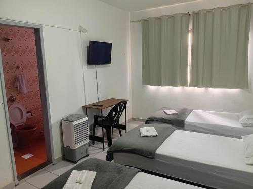 a bedroom with two beds and a desk with a television at Pousada Central Itabirito in Itabirito