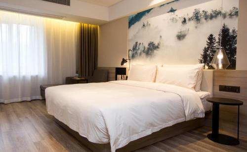 a bedroom with a white bed and a painting on the wall at Atour Hotel Hefei Hitech Avenue in Hefei