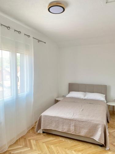 a white bedroom with a bed and a window at Apartmani Dora in Mataruška Banja