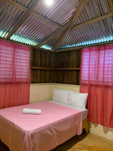 a bedroom with a bed with pink sheets and red curtains at Quisqueya in Arroyo Chico Arriba