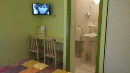 une salle de bain avec un lavabo et une télévision au mur dans l'établissement Maison Hôtel Aux Cerisiers, à La Forêt-Fouesnant