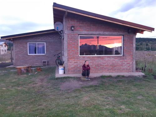a woman sitting in front of a brick house at CASA Los Tres Picos in Cholila