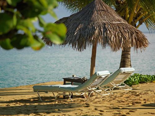 two chairs and a table under a straw umbrella on a beach at Jamaica Inn in Ocho Rios