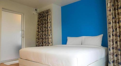 a bedroom with a blue wall and a white bed at Baan Kula Mahasarakam in Ban Nong Chik