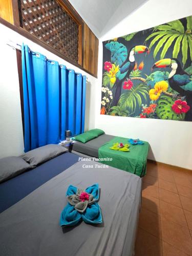 two beds in a room with blue curtains and a painting at Plaza Tucanito - jungle up your life in Cahuita