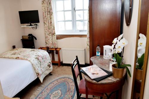 a bedroom with a bed and a desk with a table with flowers at The Inglenook Hotel in Bognor Regis