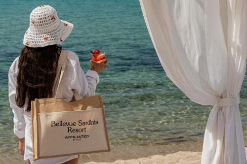 a woman standing on the beach with a bag of food at Bellevue Sardinia Resort, Affiliated by Meliá in Valledoria