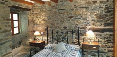 a bedroom with a stone wall with a bed and two lamps at A Casa da Zalaroia, para amantes de la naturaleza in San Mamed