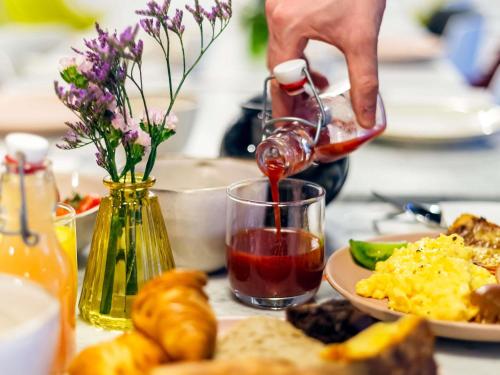 a person pouring red wine into a glass with food at Mercure Paris Alesia in Paris