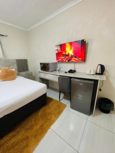 a bedroom with a bed and a desk with a monitor on the wall at Parklane Bed and breakfast in Gaborone