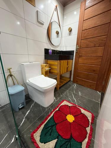 a bathroom with a toilet and a red flower rug at Recanto Pin in Alfredo Chaves