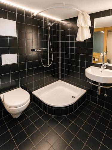 a black tiled bathroom with a toilet and a sink at Klösterli Malters in Malters