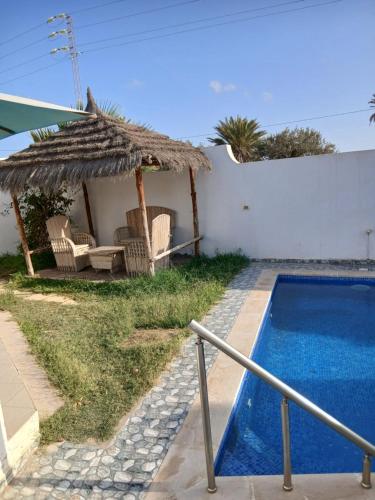 a villa with a swimming pool and a straw umbrella at Ridha in Djerba
