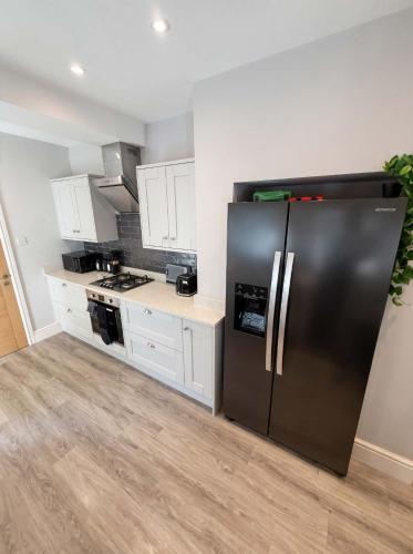 a kitchen with a black refrigerator and white cabinets at Bright 2-Bed Garden Flat Central Guildford in Purley
