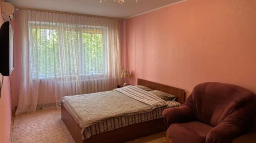 a bedroom with a bed and a chair and a window at Nice Apartment in Kyiv