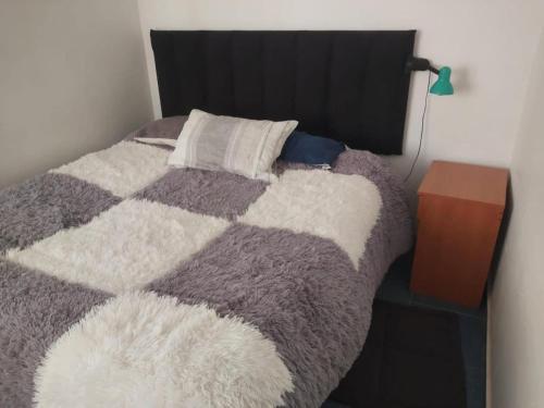 a bed with a gray and white blanket and a night stand at Hostal D&N servicios 