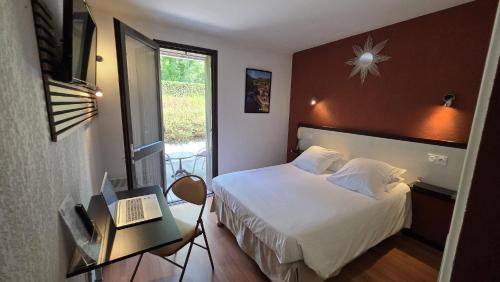 a bedroom with a bed and a desk with a laptop at Hôtel Les Gabarres in Tour-de-Faure