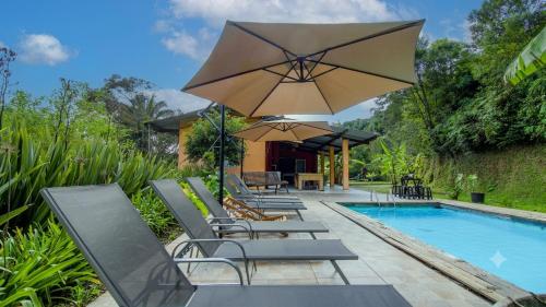 a pool with chairs and an umbrella next to a swimming pool at Sitio Chacara Piscina Aquecida Acesso Asfaltado in Juquitiba