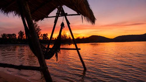 a sunset over a body of water with a hammock at Mangrove Beach Bungalows in Koh Rong Sanloem
