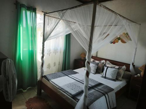 a bedroom with a canopy bed with green curtains at Le tournesol Belle villa in Maroantsetra Airport