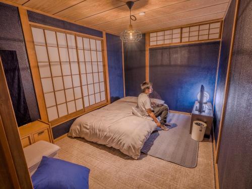 a man sitting on a bed in a room at 天然温泉付 一棟貸し最大12名 近隣施設事前予約で バーベキュー 花火 和羽灯屋 ナウヒヤ in Fuefuki