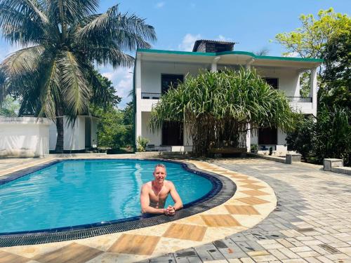 a man laying in a swimming pool next to a house at Royal Garden in Dambulla