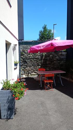 a picnic table with a pink umbrella next to a stone wall at Chambre chez sylvie in Laruns