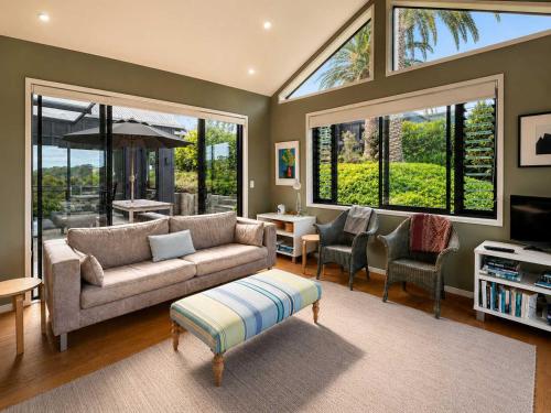 a living room with a couch and chairs and windows at Art Lovers Retreat - Stay Waiheke in Onetangi